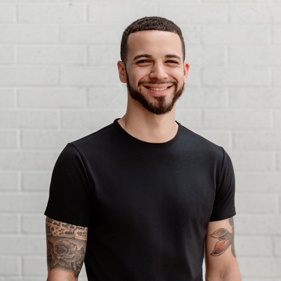 Cameron Terry smiling, in a black t-shirt against a white brick wall